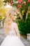 A graceful blonde bride stands under the branches of a blooming oleander near the ancient church in Prcanj