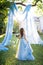 A graceful bride in a light blue dress walking to a tulle-decorated wedding arch against the background of sunset rays.