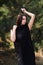 Graceful charming brunette model posing in black dress in coniferous park