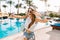 Graceful dancing girl in trendy bracelets and white hat making selfie before swimming in open-air pool. Gorgeous young