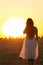 Graceful silhouette figure of young woman walking in field at sunset, beautiful romantic girl with long hair outdoors