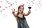 Graceful, smiling young brunette girl in party hat with glass of red wine dancing under confetti and laughing, white isolated