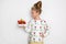 Gracious little girl with blond hair and blue eyes standing on a white background wearing a sweatshirt and a strawberry