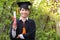 In the graden, a happy young Asian man wears graduation gowns and has a diploma