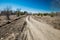 Grader rural road leading to the village. Dirt mud and dusty road through a field and trees against a clear blue sky, with tire