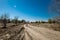 Grader rural road leading to the village. Dirt mud and dusty road through a field and trees against a clear blue sky, with tire