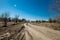 Grader rural road leading to the village. Dirt mud and dusty road through a field and trees against a clear blue sky, with tire