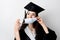 Graduate girl in medical mask at coronavirus covid-19 period. Woman with master degree in black graduation gown and cap