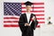 Graduate male student in a gown holding a diploma in front of USA flag