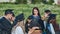 Graduates in black suits eating pizza in a city meadow.