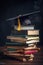 Graduation cap and gown at the top of tall textbooks stack, the symbol of wisdom. AI generative image