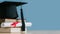 Graduation day.A mortarboard and graduation scroll on stack of books with blue background.Graduation day.Education learning