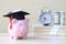 Graduation hat on blue piggy bank with stack of coins money on wooden background, Saving money for education concept