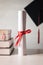 A graduation hat or mortarboard and diploma certificate paper tied with red ribbon on a stack of  books with empty space slightly