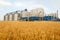 Grain elevator in front of wheat field. Flour or oil mill plant. Silos near farmland. Agriculture theme, a harvesting