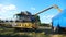 Grain harvester working in agriculture environment loading wheat grains in truck. Yellow dry kernels falling from