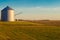 Grain silo in rural harvested field reflects early morning light just after sunrise