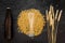 Grains and ears of malting barley near beer bottle on black background top view copyspace