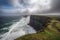 grand coastal cliff with roaring sea below, and misty clouds in the sky