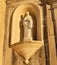 Grand stone statue of a priest standing atop a wall above a doorway containing a niche