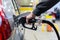 Granddad`s hand in black jacket refueling gray metallic car on gas station at night - close-up with selective focus