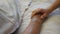 Granddaughter holds and comforts hand of her grandmother in medical clinic. Girl gently strokes wrinkled arm of sick