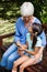 Granddaughter sitting with mobile phone looking at grandmother on wooden bench