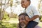 Grandfather Carries Grandson On Shoulders During Walk In Park