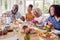 Grandfather Carving As Multi Generation Family Sit Around Table At Home And Enjoy Eating Meal