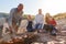 Grandfather Cooking As Multi-Generation Family Having Evening Barbecue Around Fire On Beach Vacation