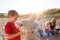 Grandfather Cooking As Multi-Generation Family Having Evening Barbecue Around Fire On Beach Vacation