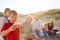 Grandfather Cooking As Multi-Generation Family Having Evening Barbecue Around Fire On Beach Vacation