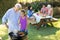 Grandfather and granddaughter preparing barbecue while family having meal