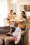 Grandfather With Granddaughter Sitting On Sofa At Home Watching Movie With Family In Background