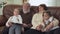 Grandfather and grandmother sitting on leather sofa in modern living room with two small girls near. Adult man reading