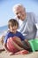 Grandfather And Grandson Building Sandcastle On Beach