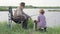 Grandfather and Grandson During Fishing On River. Sit together in field with fishing rod
