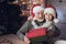 Grandfather and grandson in Santa Claus`s hats at night at home. Granddad is giving boy present.