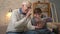 Grandfather and grandson are sitting on the sofa using a tablet, waving their hand in the video chat, greeting, smiling