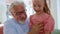 Grandfather talking with granddaughter at home. Girl sitting on grandfather laps