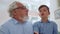 Grandfather talking grandson in room. Cheerful boy sitting on grandparent laps