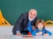 Grandfather teacher with pupil at back of classroom at the elementary school. Individual teaching. Portrait of senior