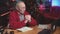 Grandfather works sitting at table with books and laptop in living room