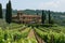 A grandiose house, nestled atop a lush green hill, commands attention with its imposing presence, A Tuscan villa surrounded by