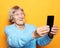 Grandma in blue sweater smiles and takes a selfie over yellow background