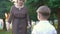 Grandma comes up to her grandson and gives him a book, sunset in the park