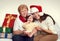 Grandma, daughter and granddaughter dressed in santa hat with gift boxes sit on sofa, white background. New year eve and christmas