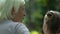 Grandmother giving advices to cute granddaughter, relaxing on bench in park