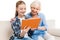 Grandmother and grandchild using digital tablet and sitting on sofa