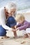 Grandmother And Granddaughter Looking at Shell On Beach Together